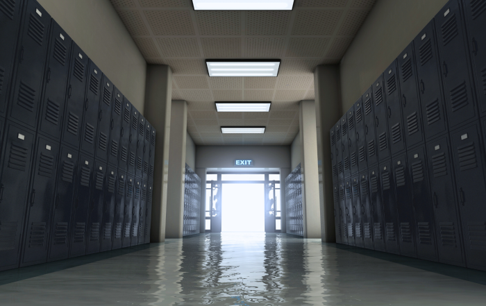 Photo of an unlit hallway in a school with lockers on both sides of the walls, where a door is open at the end of the hall and light shines out